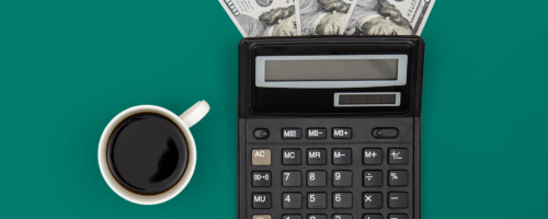 dolar bills under a calculator and a cup of black coffee next to it