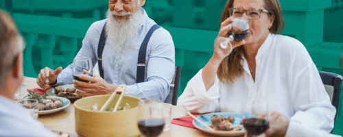 elegancki starszy mężczyzna z siwą brodą siedzi przy stole z innymi ludźmi podczas lunchu biznesowego